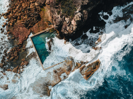 Aerial view early morning light with ocean waves flowing over rocks around North Curl Curl ocean rock pool during storm.の写真素材