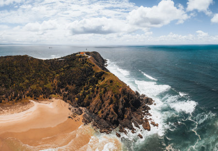 Byron Bay lighthouse high on the rocky headland - the most eastern point of Australian continent facing Pacific ocean in elevated aerial seascape above coast.の写真素材