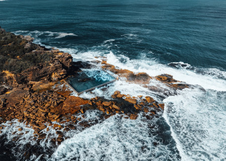 Aerial view early morning light with ocean waves flowing over rocks around North Curl Curl ocean rock pool during storm.の写真素材