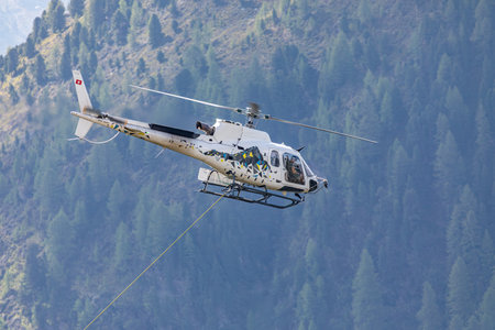 Close-up of a helicopter flying over the forest with attached transportastion rope in swiss alpsの写真素材