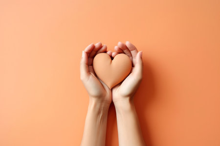 two hands over a orange lay flat holding a heartの素材