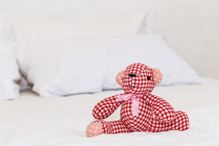 Red bear doll on white bedの写真素材