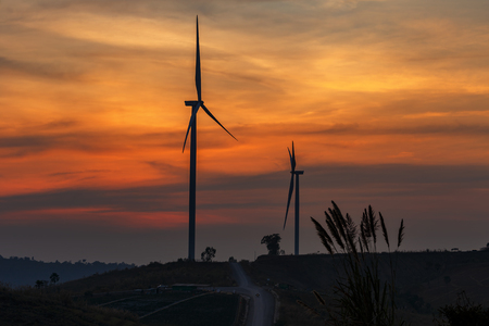 Silhouette wind turbine farm over moutain with orange sunset and cloud in blue twilight sky