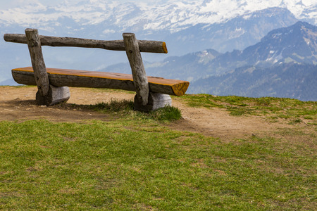 Wooden bench on green grass with view of snow on peak of high mountain, Rigi kulm Luzern Switzerland Europeの写真素材