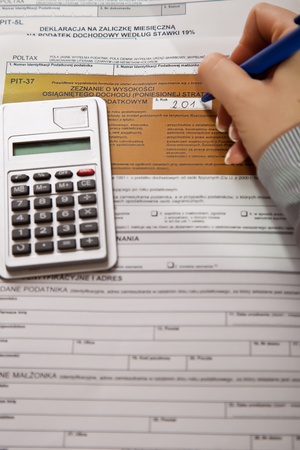 Woman hand filling income tax forms with calculator
