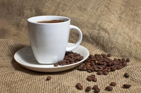 Cup of coffee and coffee beans on jute background の写真素材