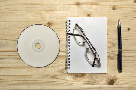 Blank stationery set : glasses CD notebook and pencil on wooden table.