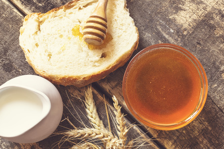 Honey in a jar, slice of bread, wheat and milk on an old vintage planked wood table from above. Rural or rustic style breakfast concept.の写真素材