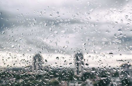 Rain drops on window glass outside texture background water of wonderful heavy rainy day with sky clouds at cityの写真素材