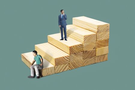 Miniature people: two business man stands and sitting down on wooden stairs.