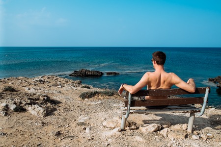 Rear view portrait of white man sitting relaxed on a bench and looking at the sea, man on a holiday. Cyprusの写真素材