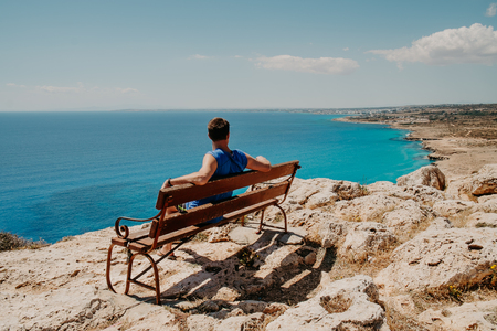 Rear view portrait of white man sitting relaxed on a bench and looking at the sea, man on a holiday. Cyprusの写真素材