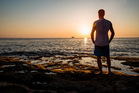 man looks at the sunset at the sea