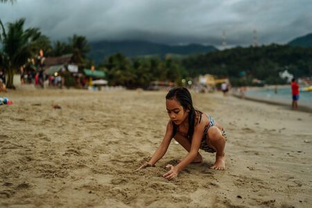 Nov 2016, Mindoro island. Asian kids playng in shallow water ahead of oncoming waves of the sea at sunset, Island, Philippinesのeditorial素材