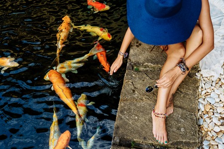 girl in the hat sitting near the water with golden carps. Philippines, Boracayの写真素材