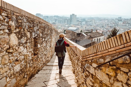 A young tourist with a backpack shoots video on smartphone, standing on a Fortress wall (Passeig de...