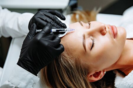 Portrait of female patient having modern noninvasive procedure of rhinoplasty, Doctor injects substance in patient nose, Aesthetic corrective treatments conceptの写真素材