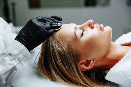 Portrait of female patient having modern noninvasive procedure of rhinoplasty, Doctor injects substance in patient nose, Aesthetic corrective treatments conceptの写真素材