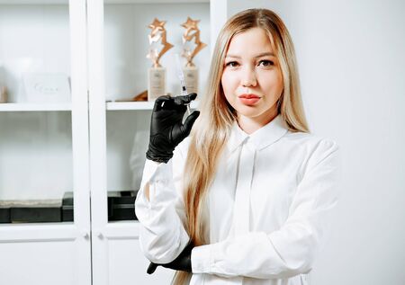 Doctor in pink gown and gloves holds syringe in medical office, ready for making injections. Cosmetologist before anti ageing procedure for her client. Aethetic medicine, skin care and cosmetology.の写真素材
