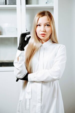 Doctor in pink gown and gloves holds syringe in medical office, ready for making injections. Cosmetologist before anti ageing procedure for her client. Aethetic medicine, skin care and cosmetology.の写真素材
