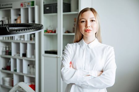 portrait of smiling cosmetologist in white coat standing at empty massage table in salonの写真素材
