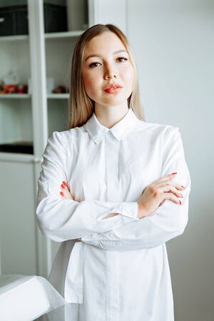 portrait of smiling cosmetologist in white coat standing at empty massage table in salonの写真素材