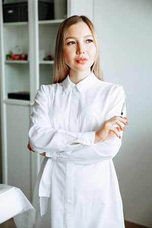 portrait of smiling cosmetologist in white coat standing at empty massage table in salonの写真素材