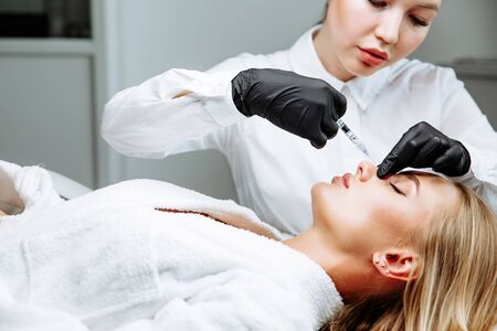 The doctor cosmetologist makes prick in the nose to correct the hump of a beautiful woman in a beauty salon. Cosmetology skin care.の写真素材