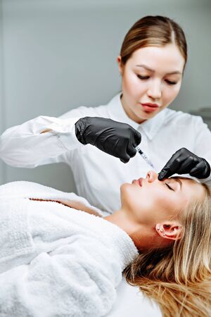 The doctor cosmetologist makes prick in the nose to correct the hump of a beautiful woman in a beauty salon. Cosmetology skin care.の写真素材