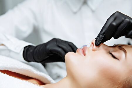 The doctor cosmetologist makes prick in the nose to correct the hump of a beautiful woman in a beauty salon. Cosmetology skin care.の写真素材