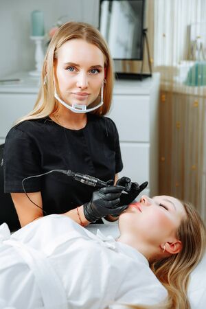 Young woman having permanent makeup on lips in beautician salonの写真素材