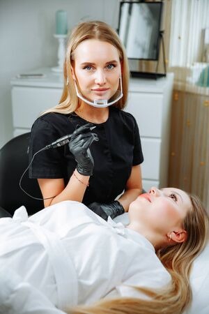 Master beautician, blonde, bent over lying European girl and makes her permanent lip makeup in the beauty salon. Close up. The view from the top. Vertical orientation of the imageの写真素材