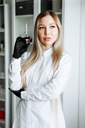 Doctor in pink gown and gloves holds syringe in medical office, ready for making injections. Cosmetologist before anti ageing procedure for her client. Aethetic medicine, skin care and cosmetology.の写真素材