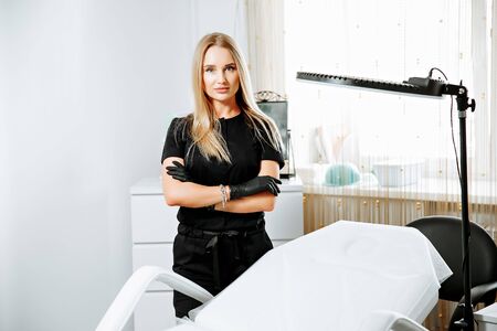 Caucasian cosmetologist standing in black coat near placard with drawn eye at cosmetology cabinet. Concept of qualitative medical worker, beauty salon and permanent makeup.の写真素材