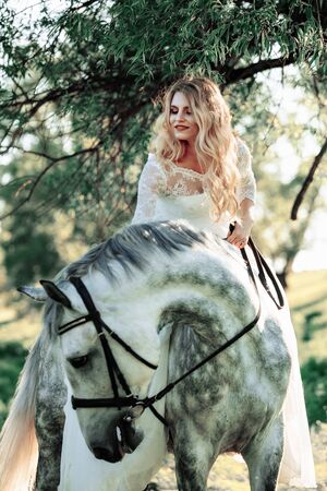 Beautiful and stunning bride, riding a horse in the nature, on her wedding dayの写真素材