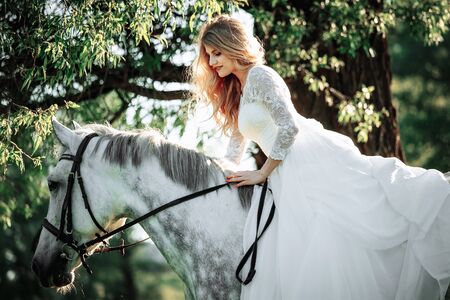 Fashionable woman riding a horse in sunny day. Long curly hair. Fashion colors.の写真素材