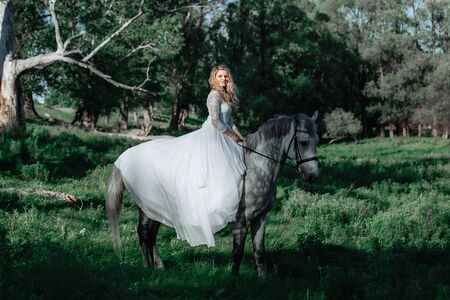 Beautiful and stunning bride, riding a horse in the nature, on her wedding dayの写真素材