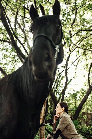 Fashionable portrait of a beautiful young woman and black horseの写真素材