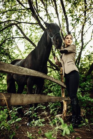 Fashionable portrait of a beautiful young woman and black horseの写真素材