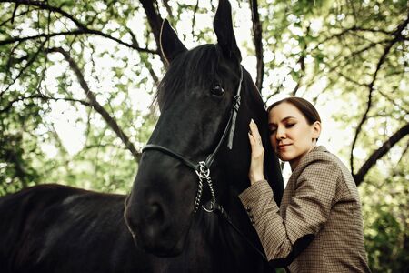 Fashion photoshoot of beautiful woman and black horse. Outdoor shot, sport and fashion concept.の写真素材