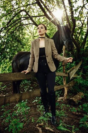 Fashion photoshoot of beautiful woman and black horse. Outdoor shot, sport and fashion concept.の写真素材