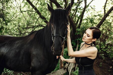 Fashion photoshoot of beautiful woman and black horse. Outdoor shot, sport and fashion concept.の写真素材