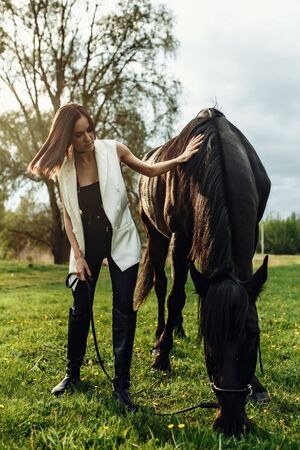 Fashion photoshoot of beautiful woman and black horse. Outdoor shot, sport and fashion concept.の写真素材