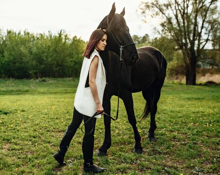 Fashionable portrait of a beautiful young woman and black horseの写真素材