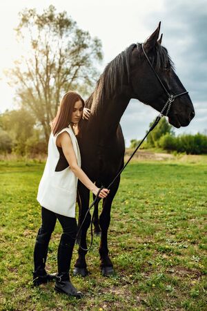 Fashion photoshoot of beautiful woman and black horse. Outdoor shot, sport and fashion concept.の写真素材
