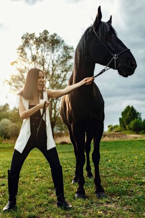 Fashionable portrait of a beautiful young woman and black horseの写真素材