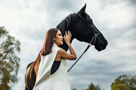 Fashionable portrait of a beautiful young woman and black horseの写真素材