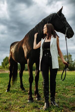 Fashionable portrait of a beautiful young woman and black horseの写真素材