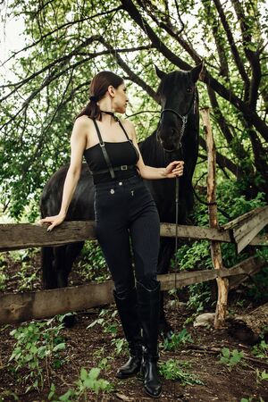 Fashionable portrait of a beautiful young woman and black horseの写真素材