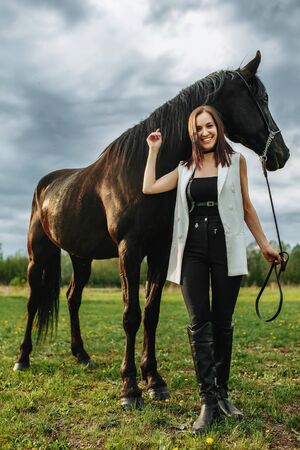 Fashion photoshoot of beautiful woman and black horse. Outdoor shot, sport and fashion concept.の写真素材